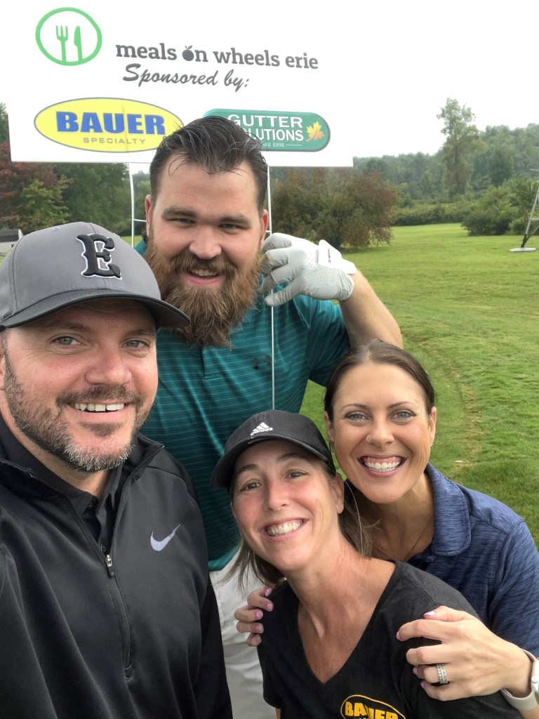 Bauer employees at golf tournament taking selfie with sign